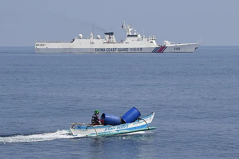 FILE: This photo taken on 20 September 2023 shows a Philippine fisherman aboard his outrigger boat sailing past a Chinese coast guard ship near the Chinese-controlled Scarborough Shoal in waters of the disputed South China Sea. China, which claims sovereignty over almost the entire South China Sea, snatched control of Scarborough Shoal from the Philippines in 2012. Since then, it has deployed coast guard and other vessels to block or restrict access to the fishing ground that has been tapped by generations of Filipinos. (Photo by Ted ALJIBE / AFP)