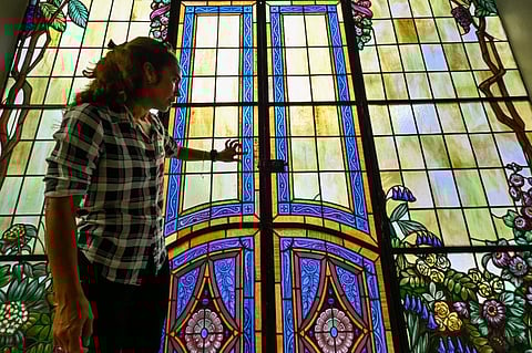 The teacher of stained glass restoration at the School Workshop of Havana, Mirell Vázquez, talks in front of a historical stained glass door on November 7, 2023, in Havana. The magic of the union of light and colorthe art of stained glasshas flourished over the centuries in Havana, where restoration work is helping to preserve this jewel of Cuban architecture. (Photo by ADALBERTO ROQUE / AFP)