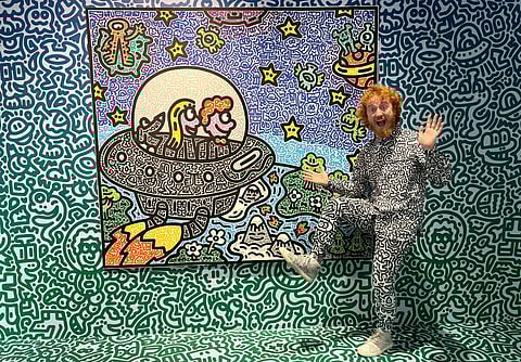 This photo taken on 16 November 2023 shows British artist Sam Cox, better known as Mr. Doodle, posing for a picture with his piece "The Doodles Leave Earth" at Pearl Lam Galleries in Hong Kong. (Photo by Dene CHEN / AFP)