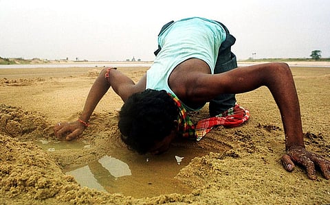 FILE PHOTO: A laborer in a closeby construction site, quenches his thirst from a water-hole dug at a dried-up river bed at Birbhum in the eastern Indian state of West Bengal. (Photo by DIBYANGSHU SARKAR / AFP)