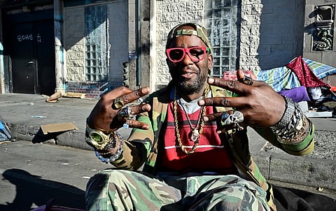 FILE PHOTO: A homeless man gestures while sitting on a luggage bag along a downtown Los Angeles street lined with tents housing the homeless on 22 November 2023 in Los Angeles, California, where skyrocketing rents in recent years has led to an increasing rise in the number of unhoused people. (Photo by Frederic J. BROWN / AFP)