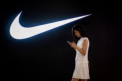 FILE PHOTO: A woman browses her phone while walking past a Nike logo inside a shopping mall. (Photo by NICOLAS ASFOURI / AFP)