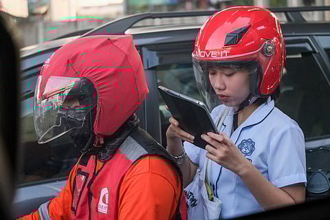 A passenger in a motorcycle taxi looks at her tablet while riding down Sergio Osmeña Road in Manila on 6 December 2023. | 📷KING RODRIGUEZ