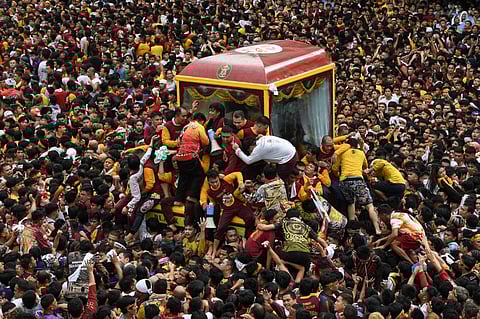 Catholic devotees climb into a glass-covered carriage carrying the so-called Black Nazarene statue as they try to touch it during an annual religious procession in Manila on 9 January 2024. (Photo by Ted ALJIBE / AFP)