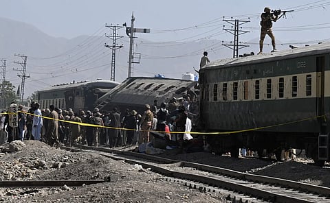 A soldier aims his weapon from atop a carriage as security officials inspect derailed train carriages after an explosion targeted a train in Quetta on May 24, 2026.