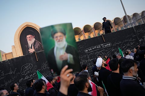 A mourner holds a portrait of the late Iranian Supreme Leader Ayatollah Ali Khamenei as he walks past a wall bearing messages, including one in English that reads "We will kill Trump," during the funeral ceremonies for Khamenei and members of his family at the Imam Khomeini Mosalla Grand Mosque in Tehran, Iran, 4 July 2026.