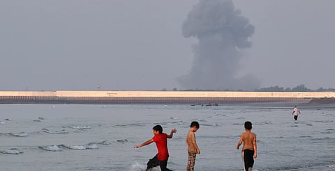Three boys play in the shallow waters of the Strait of Hormuz, as a plume of smoke rises from an explosion in the background, off Bandar Abbas, Iran, Monday, July 13, 2026.