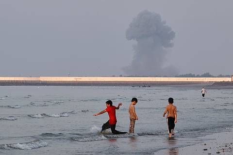 Three boys play in the shallow waters of the Strait of Hormuz, as a plume of smoke rises from an explosion in the background, off Bandar Abbas, Iran, 13 July 2026.