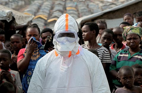 A health worker in personal protective equipment stands near displaced people waiting for the burial of suspected Ebola victims at the Kigonze displaced persons camp, one month after an outbreak was declared, in Bunia, eastern Democratic Republic of Congo, June 18, 2026.