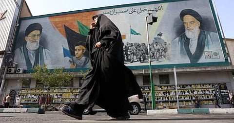 A woman walks past a mural featuring Iran's late supreme leaders in Tehran