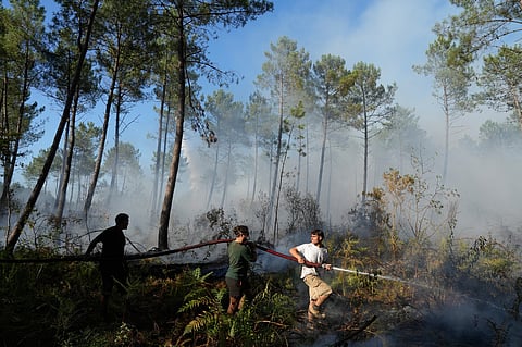 A group hold a firehose and try to suppress a fire near Lacanau, as wildfires rage outside Bordeaux, France, Monday, July 27, 2026.