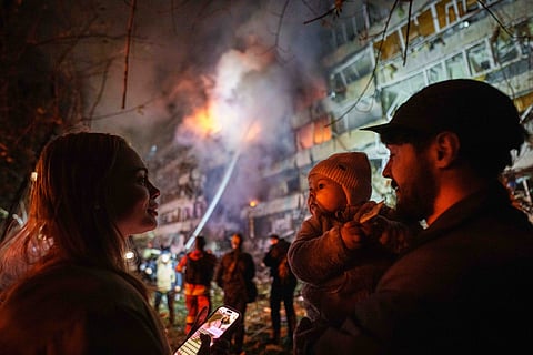Victoria Deineko, her husband Ievhen Deineko and their daughter Mia look at a multi-story residential building damaged in a Russian missile strike in Kyiv, Ukraine, Tuesday, Oct13, 2026.