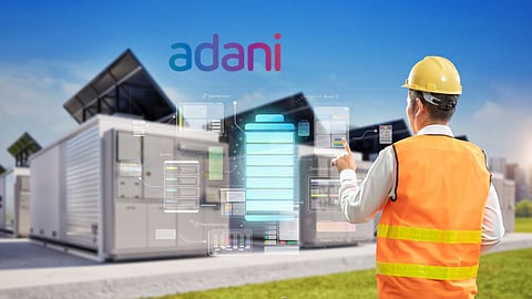 Engineer wearing safety gear monitors a smart energy storage facility with solar panels, as the Adani logo appears above—symbolising the company’s focus on renewable energy and advanced battery technology.