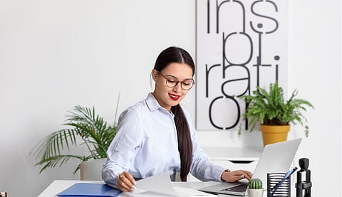 Young Woman Working on Laptop at Desk with Documents and Notebook in Modern Bright Workspace