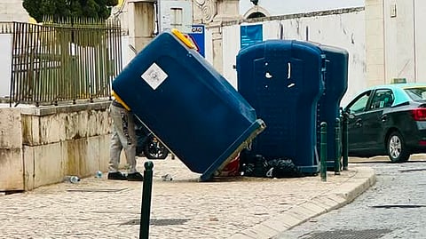Um 'mineiro do lixo', fotografado por um habitante local, vira um contentor de reciclagem em Santos-o-Velho, Lisboa, preparando-se para começar a despejar o seu conteúdo e aproveitar as embalagens que poderá trocar.