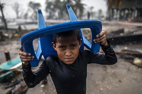 भारी बारिश में अपने आप को बचाने के लिए कुर्सी के नीचे छिपने का असफल प्रयास करता बच्चा; फोटो: यूनिसेफ/यूएन0372375/ओcon/एएफपी-सर्विसेज