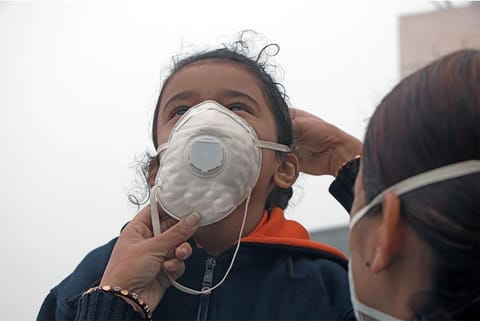 बढ़ते प्रदूषण में अपनी बच्ची की मास्क पहनने में मदद करती एक मां; फोटो: आईस्टॉक