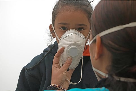 हवा में घुले जहर से बचाने के लिए अपने बच्चे को मास्क पहनने में मदद करती मां; फोटो: आईस्टॉक