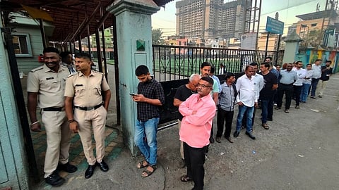 Police personnel stand guard as people wait in a queue to cast votes during the Navi Mumbai Municipal Corporation (NMMC) elections, at a polling station at Kopar Khairane, in Navi Mumbai, Maharashtra, Thursday, Jan. 15, 2026.