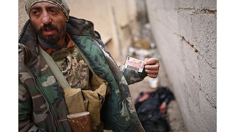 A Syrian government soldier displays the ID of a dead civilian found in the street after government forces seized the strategic town of Taqba in eastern Syria, as part of an ongoing push against Kurdish-led forces.
