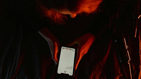 A person illuminated by a warm, dim light scrolls through their phone in a dark room
