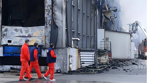 Workers walk past a burned building after an explosion and fire at a cookie factory in Trikala, central Greece