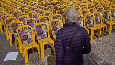 A woman walks by chairs with photos of Ran Gvili, the final hostage in Gaza who was killed while fighting Hamas militants during the Oct. 7, 2023 attack, a day after his remains were recovered, in a plaza known as Hostages Square, in Tel Aviv, Israel