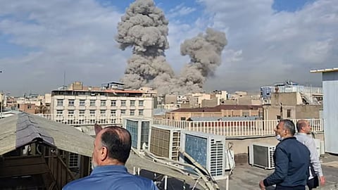 People watch as smoke rises on the skyline after an explosion in Tehran, Iran