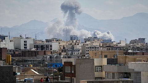 People watch from a rooftop as a plume of smoke rises after a strike in Tehran, Iran.