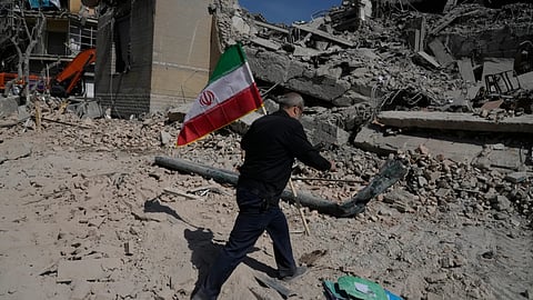 A man carries an Iranian flag to place on the rubble of a police facility struck during the US-Israeli military campaign in Tehran, Iran