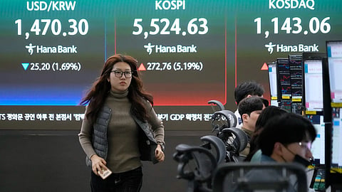 A currency trader passes by a screen showing the Korea Composite Stock Price Index (KOSPI), rear center, and the foreign exchange rate between U.S. dollar and South Korean won, rear left, at the foreign exchange dealing room of the Hana Bank headquarters in Seoul, South Korea, Tuesday, March 10, 2026.