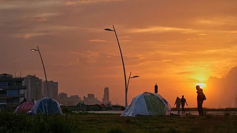 People walk past tents sheltering people displaced by Israeli airstrikes at a public space along the Beirut waterfront at sunset in Beirut, Lebanon