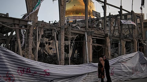 Pedestrians look at a destroyed building within the Grand Hosseiniyeh, with the mosque visible in the background, which officials at the site say was hit by U.S.-
Israeli airstrikes