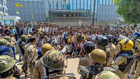 Security personnel stand guard as factory workers stage a protest demanding a hike in wages, in Noida, Gautam Buddh Nagar district, Uttar Pradesh, Monday, April 13, 2026
