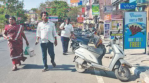 Pedestrians walk on Madhavaram High Road as pavement is encroached by shops