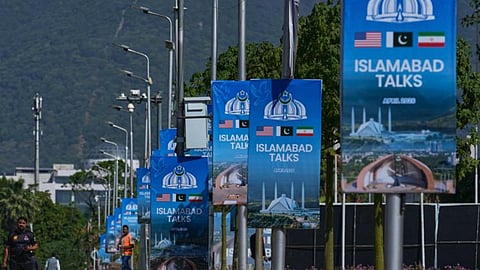 Workers walk past billboards near the Serena Hotel ahead of the second round of negotiations between the US and Iran, in Islamabad, Pakistan