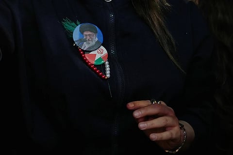 A government supporter wears badges showing a portrait of the slain Iranian Supreme Leader Ayatollah Ali Khamenei, and Iranian and Palestinian flags during a pro-government gathering at Islamic Revolution Square in Tehran, Iran, Wednesday, May 13, 2026.