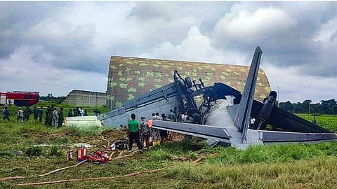 Security personnel and others stand near damaged remains of a transport aircraft of the Indian Air Force (IAF) that crashed while landing, in Jorhat district, Assam