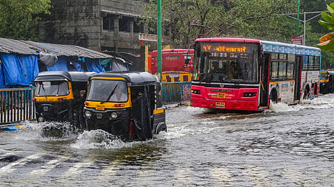 Commuters move on a waterlogged road following the rise of water level in Masunda lake due to rainfall at Thane