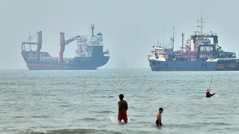 Children wade in the water with cargo ships at anchor in the background and a fisherman nearby, in the Strait of Hormuz off Bandar Abbas, Iran.