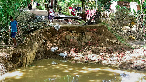 People move near the debris of a damaged house in a flood-affected area following incessant heavy rainfall, at Jhanji in Sivasagar district