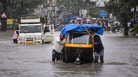Commuters wade through a waterlogged area after heavy rain, in Ahmedabad
