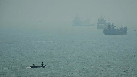A motorboat travels past commercial vessels anchored amid haze in the Strait of Hormuz off Bandar Abbas, Iran.