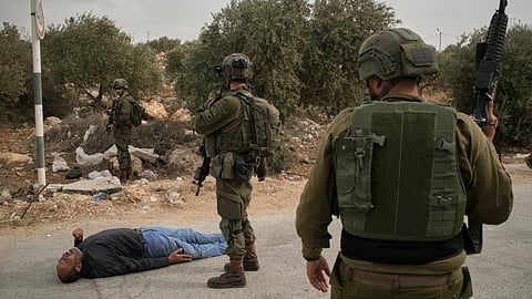 Israeli soldiers stand beside a wounded Palestinian man