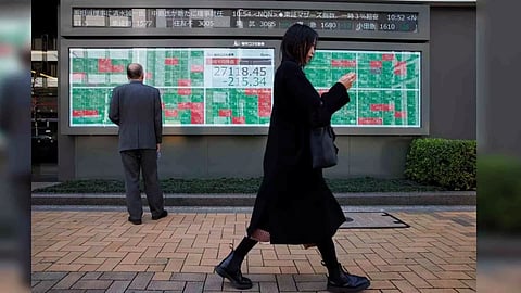 A woman walks past a man examining an electronic board showing Japan's Nikkei average and stock quotations outside a brokerage, in Tokyo, Japan (Photo: Reuters)