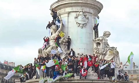 People atop a European monument waving the Algerian flag