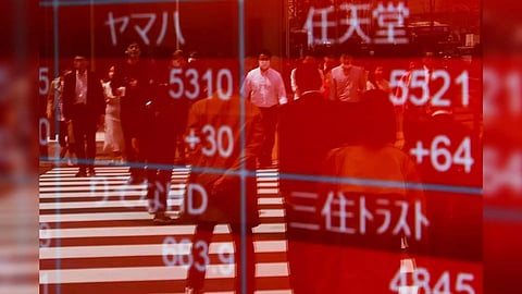 Passersby are reflected on an electric stock quotation board outside a brokerage in Tokyo