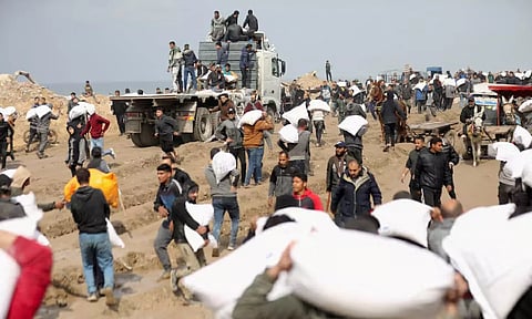 Palestinians carry bags of flour they grabbed from an aid truck near an Israeli checkpoint, in Gaza City