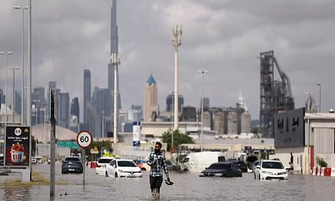 A person walks in flood water caused by heavy rains, with the Burj Khalifa tower visible in the background, in Dubai, UAE (Reuters)