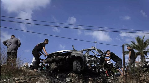 Palestinians gather around a car destroyed in a drone strike Zeita village (AP)